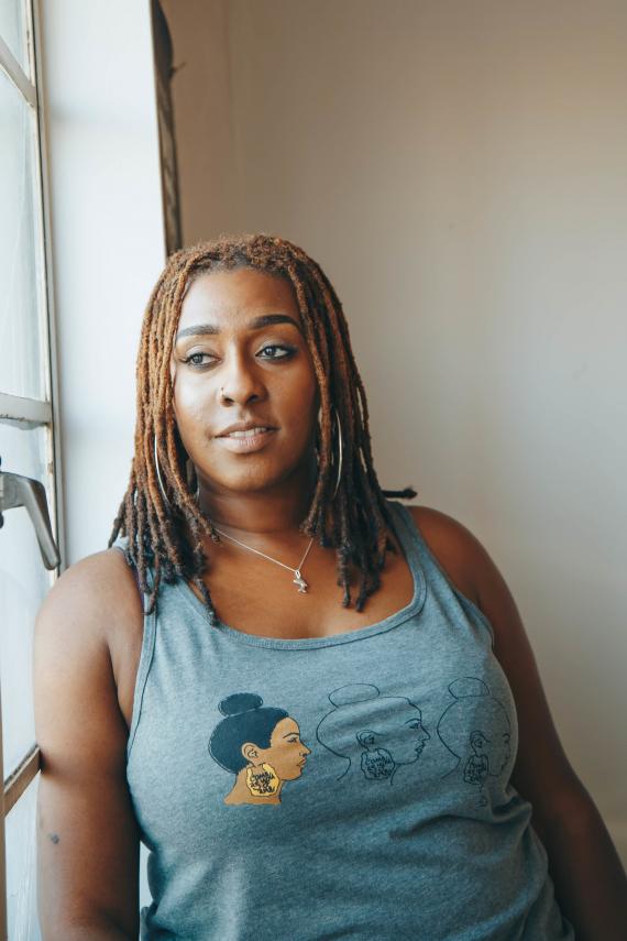 Bildtext: Foto på cool tjej med flätor i håret vid ett fönster. 